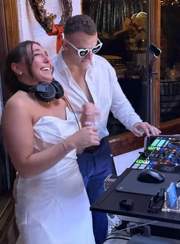 Bride and groom DJing their own wedding with headphones on while smiling behind the DJ deck at a Pittsburgh reception