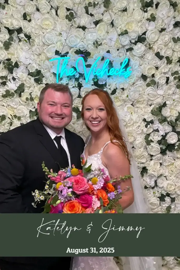 Bride and groom posing in the digital photo booth in front of a flower wall at a Pittsburgh wedding