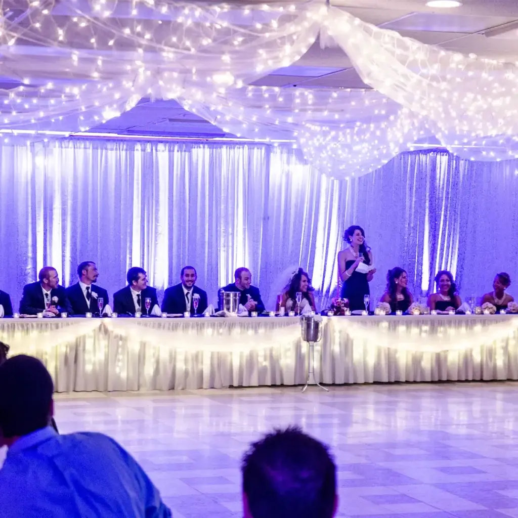 Pipe and drape backdrop with purple uplighting at a wedding reception at Rostraver Fire Hall near Pittsburgh